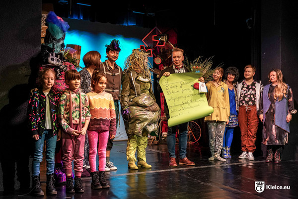 Grupa aktorów i dzieci na scenie Teatru Lalki i Aktora