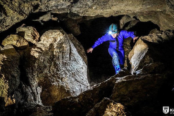 Kobieta grotołaz przemieszcza się pomiędzy ścianami jaskini.