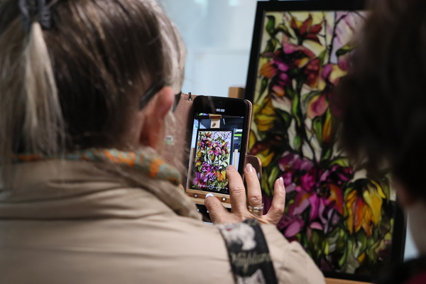 Kobieta robiąca zdjęcie obrazowi przedstawiającemu kwiaty