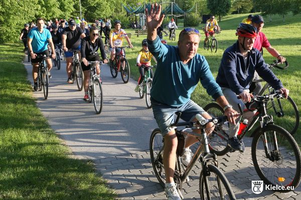 Kilkadziesiąt osób jedzie na rowerach. Na pierwszym planie mężczyzna w zielonej bluzie macha ręką. W tle fragment Strefy Relaksu w Dolinie Silnicy i drzewa.