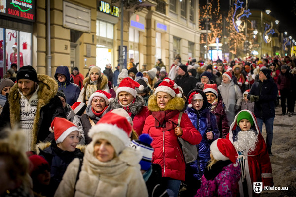 Kilkadziesiąt osób idzie w orszaku Świętego Mikołaja przez ul. Sienkiewicza. Część osób założyła mikołajowe czapki