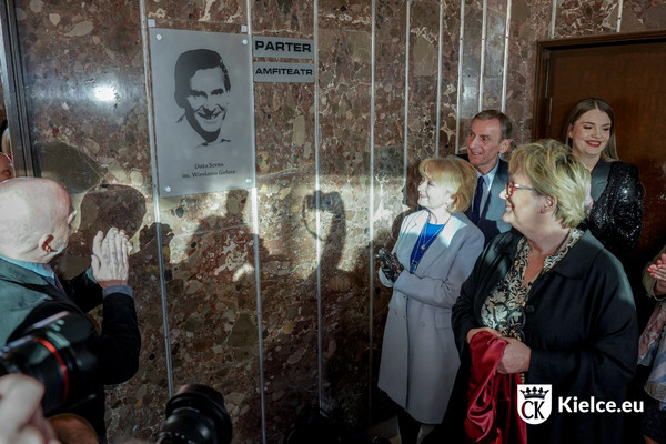 Kilka osób stojących przed tablicą ze zdjęciem Wiesława Gołasa i napisem Duże Scena im. Wiesława Gołasa.