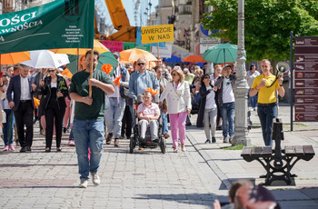 Grupa osób z niepełnosprawnościami idzie wraz z opiekunami ulicą Staszica. 