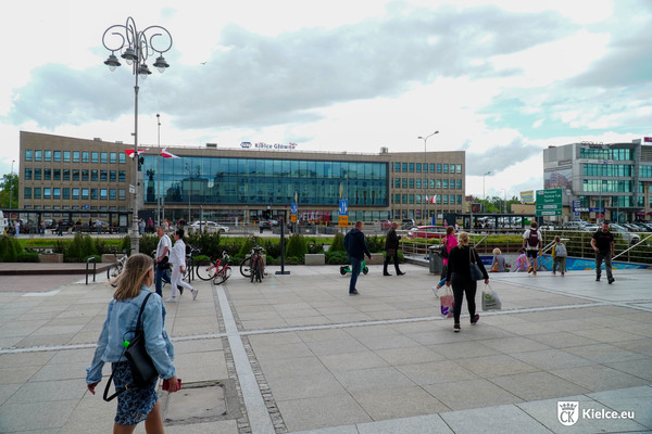 Ulica Sienkiewicza od strony dworca kolejowego, wejście do przejścia podziemnego, kilka osób przechodzi ulicą, kilka wchodzi lub wychodzi z tunelu, na drugim planie budynek dworca.