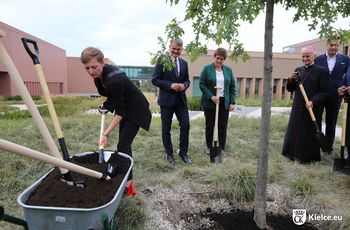 Kilka osób sadzi drzewo na dziedzińcu Kampusu Głównego urzędu Miar